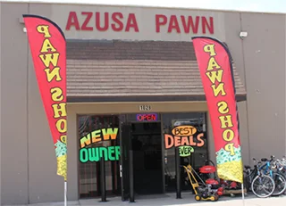 A pawn shop with grey walls, 2 red banners hanging on the wall that says "PAWN SHOP", lettering on the glass wall that says "New Owner" and "Best Deals", bicycles outside the store